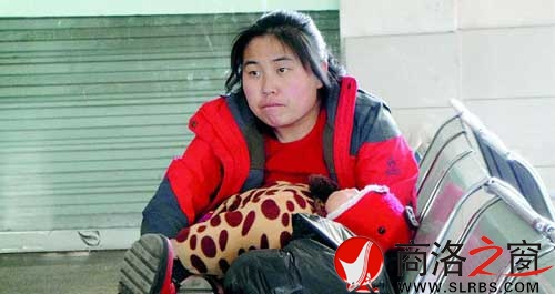 候车厅里，一位母亲抱着睡着的孩子发呆